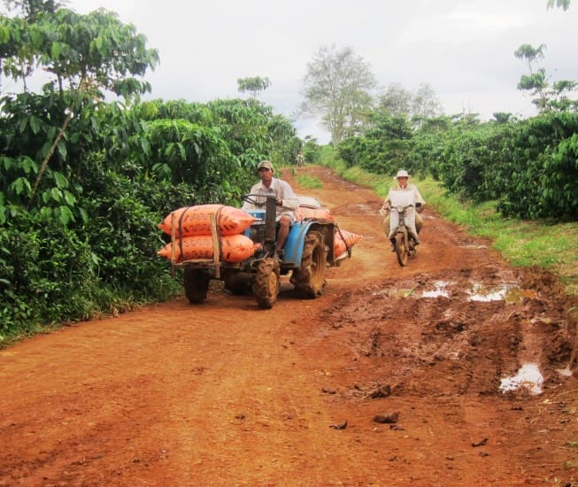 A man on a small tractor and a man on a scooter driving along a dirt road