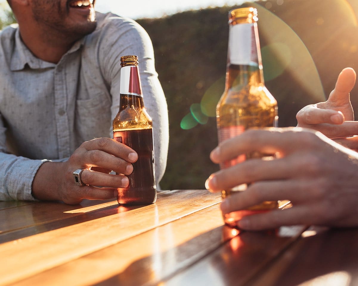 Two people sitting outdoors at wooden table having beers and talking