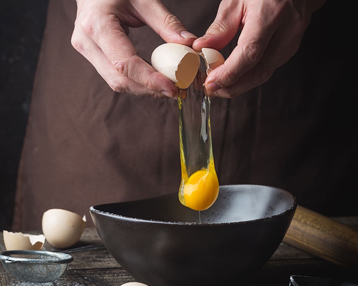 Hands breaking an egg into a bowl