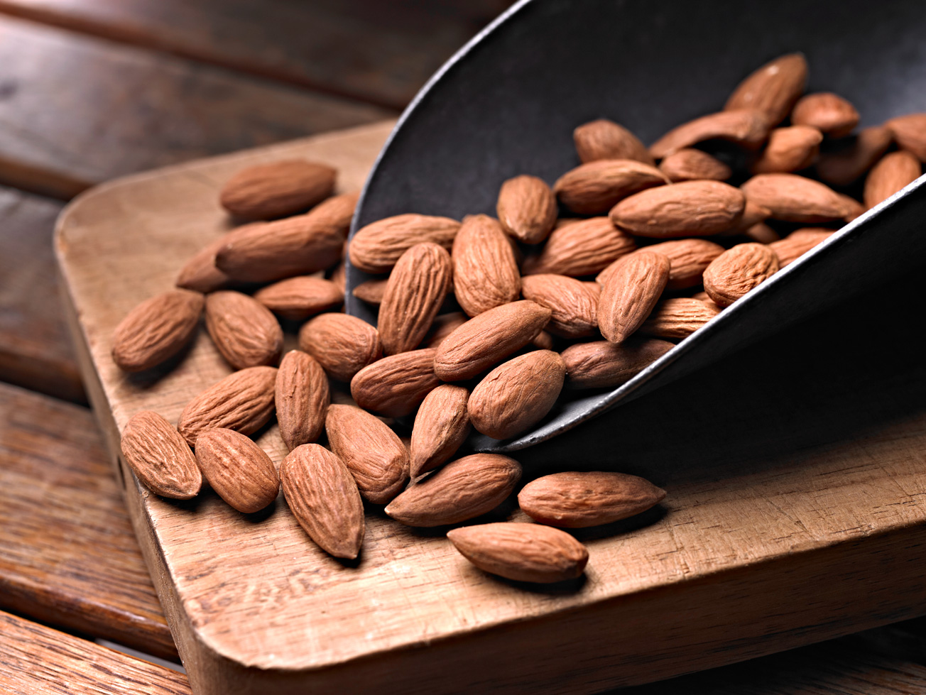 Raw almonds spilling from a metal scoop onto a wooden board – representing global almond market prices